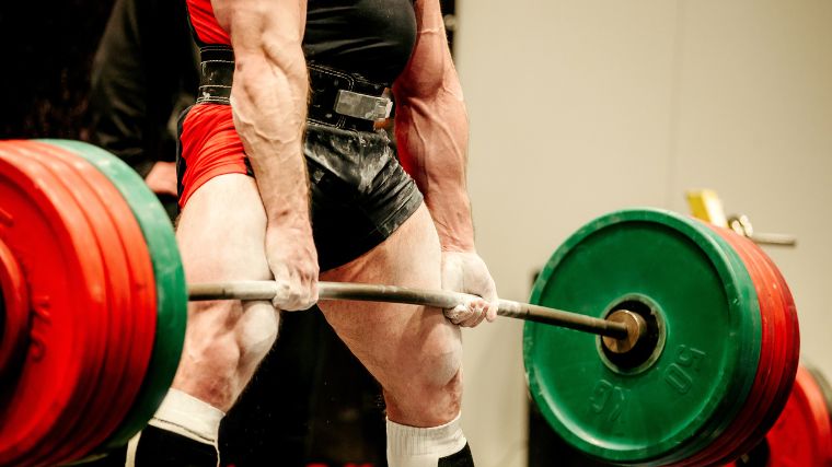 Person wearing a powerlifting singlet and lifting belt deadlifts a loaded barbell.